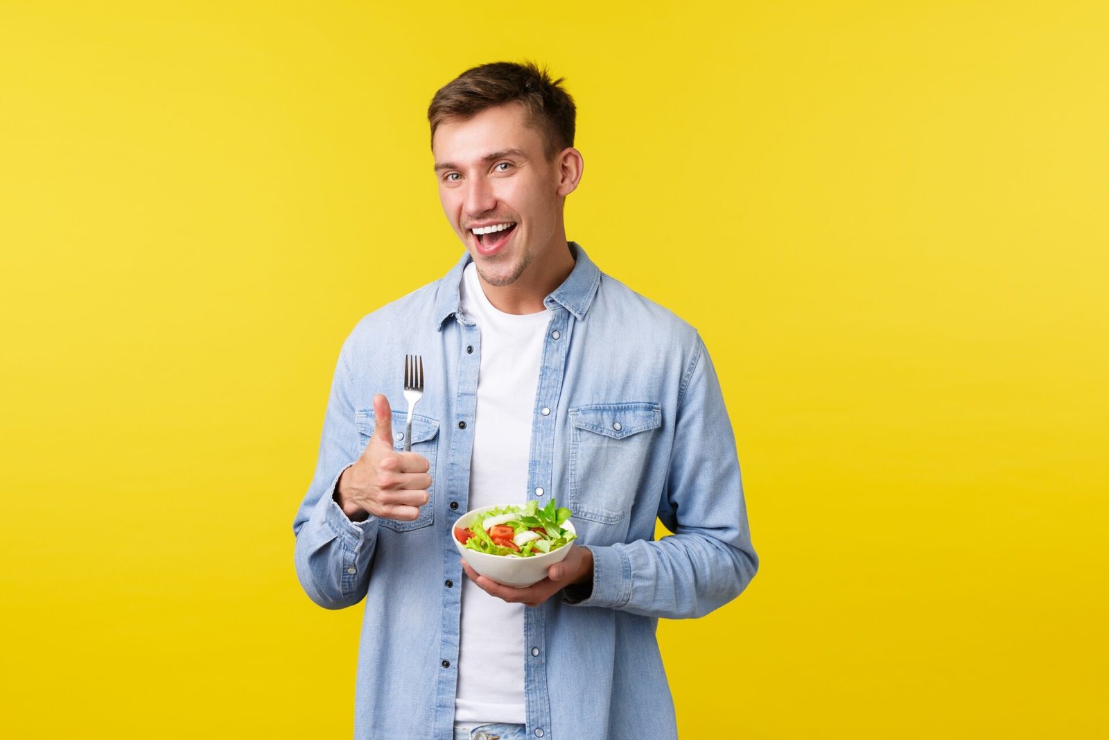 happy-smiling-man-showing-thumbs-up-satisfied-with-delicious-breakfast-eating-salad-being-on-diet-trying-stay-fit-standing-yellow-background
